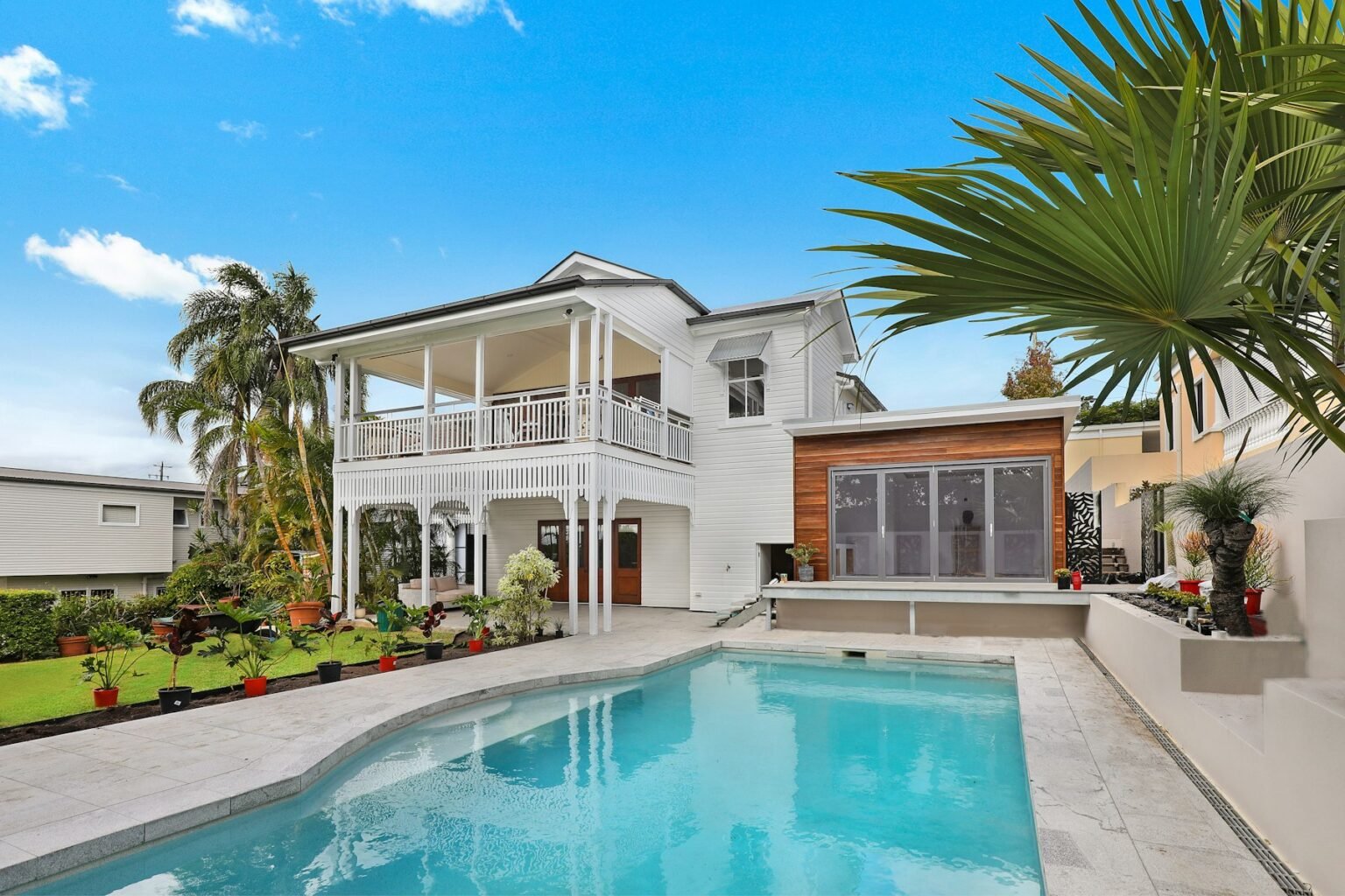Palm-lined backyard swimming pool beside a white Southern California home